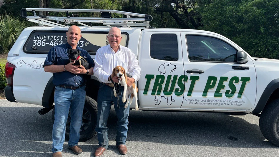 Pepe Peruyero (left) holding Raton, a patterdale breed, and Jose Tomeu (right) holding beagle Alani posing in front of a Trust Pest vehicle.